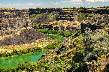 Green Snake River winds through rugged basalt cliffs of Snake River Canyon in Twin Falls, Idaho. Scenic landscape highlights dramatic geology of American West with contrast between arid canyon walls