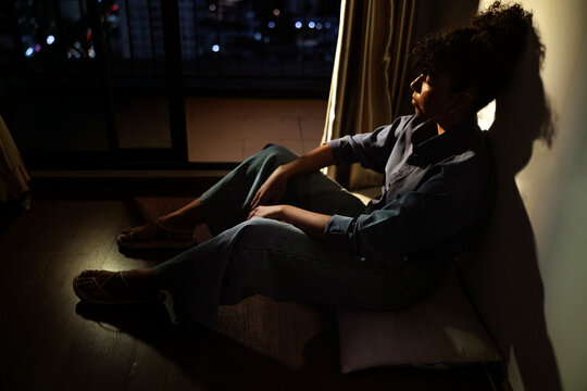 Woman sits, gazing at city lights, lost in thought.