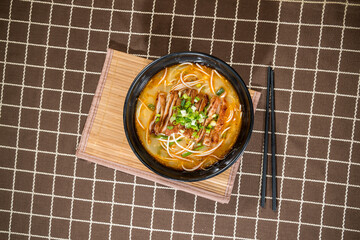 A bowl of Japanese ramen with noodles, grilled meat slices, green onions, and broth, served on bamboo mat.