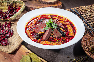 A bowl of spicy Chinese hot pot with tofu, congealed blood, mushrooms, and chili peppers in red broth, garnished with cilantro and rustic spices.