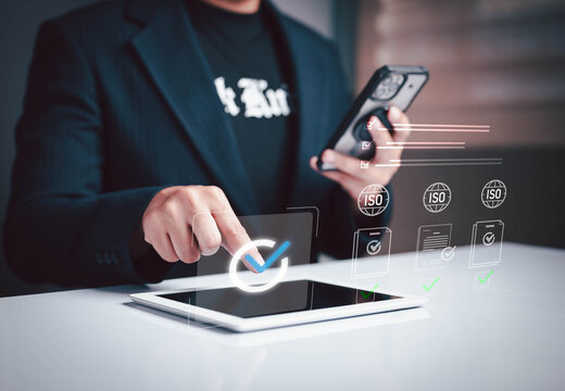 Businessman using digital tablet and smartphone to manage ISO certification documents, quality control, and compliance in smart office environment. Futuristic interface for digital workflow.