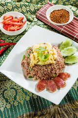 Thai-style fried rice with green beans, scrambled egg, Chinese sausage, and cucumber slices, served on white plate with chili and tomato sides.