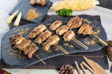 Skewers of grilled meat, chicken, and enoki mushrooms topped with dry spices and cheese, served with corn and parsley.