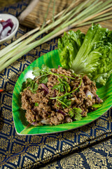 Thai larb salad with minced meat, onion, cilantro, and lettuce served on leaf-shaped plate with Thai decor.