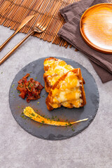 Croissant halves topped with melted cheese, served with bacon and sauce on slate plate with rustic decor.