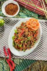 A vibrant Thai larb salad featuring minced meat, red chili, green beans, and lettuce, served with a carved carrot flower on a white plate.