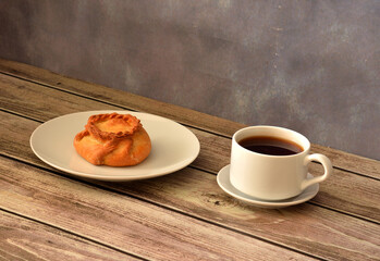Elesh, a traditional Tatar pastry stuffed with meat, served on a round plate with a cup of hot tea on a wooden table.