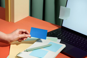 Hand holding a blue card above a notebook and laptop