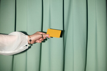 A person's hand elegantly holds a yellow card in front of a curtain
