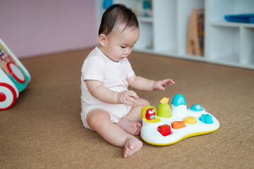 An engaged baby sits on the floor and concentrates on playing