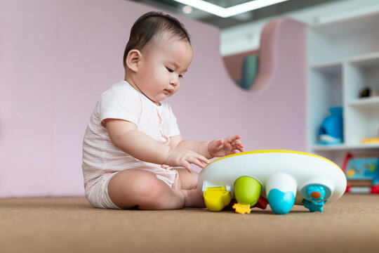 An adorable baby sits on the floor, engaging with a colorful toy