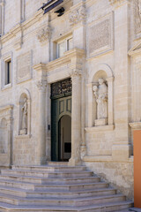 ornate stone facade and entrance of a baroque church, featuring statues in niches and a flight of steps, under bright daylight in southern italy