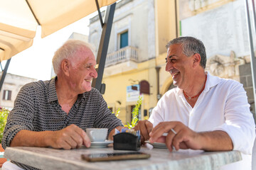 Happy gay couple enjoying coffee and laughter at a sunny outdoor cafe