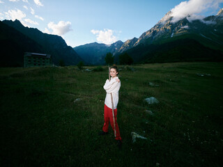 Fototapeta premium Child, girl, mountain valley landscape with open field and rugged peaks, wearing white jacket and red pants, standing confidently in a wide alpine setting for outdoor adventure