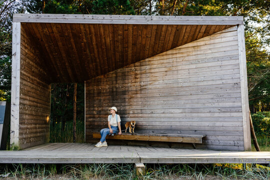 Woman and dog inside wooden shelter along forest interpretive trail