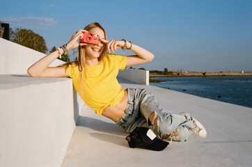 Smiling woman enjoying sunny day holding red film camera up to eye