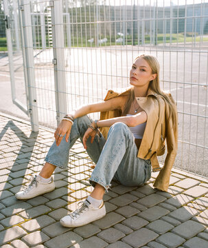 Woman in leather jacket sitting by metal fence in sunlight