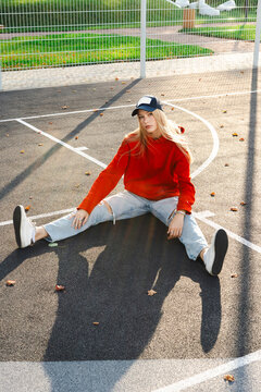 Woman sitting on outdoor basketball court in red sweatshirt