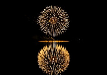 Fototapeta premium Spectacular Golden Fireworks Display Reflected in Still Water on a Dark Night Creating a Festive and Celebratory Atmosphere with Bright Lights and Vibrant Colors