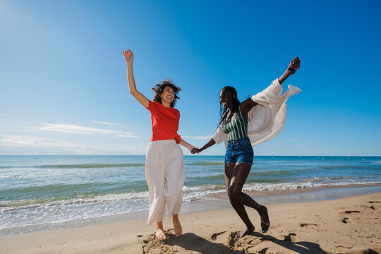 Diverse women friends jumping with joy at beach