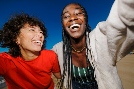 Diverse women friends laughing taking beach selfie