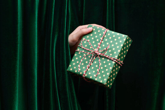 Hand holding a wrapped gift against a green velvet curtain.