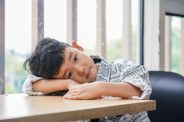 Boy resting head on table in quiet indoor space