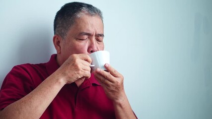 Mature asian man enjoying warm cup of coffee while savoring the moment with eyes closed