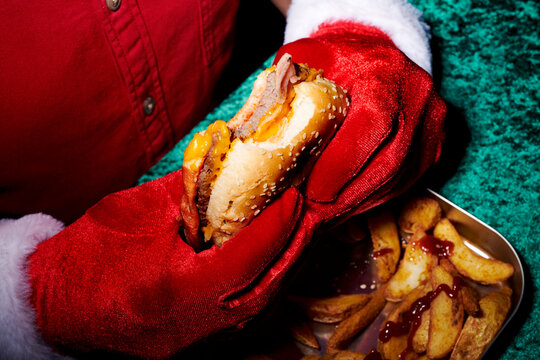 a man in santa gloves lifts a burger above potato wedges on a tray