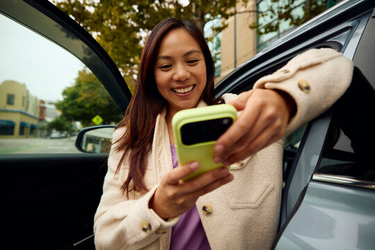 Woman smiles while texting on her phone next to the car