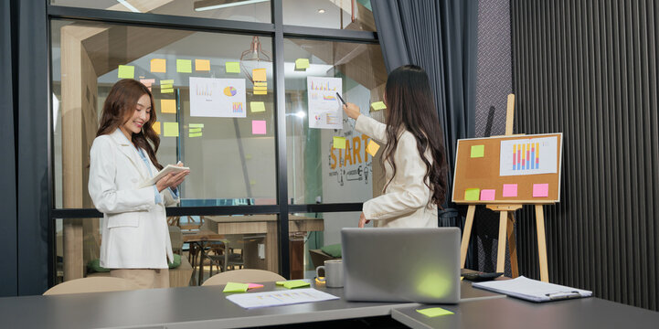 Busy business women meet, team people work project, productive meeting discussion, analyzing charts, pointing data on glass wall, reviewing corporate reports, smiling woman holds tablet