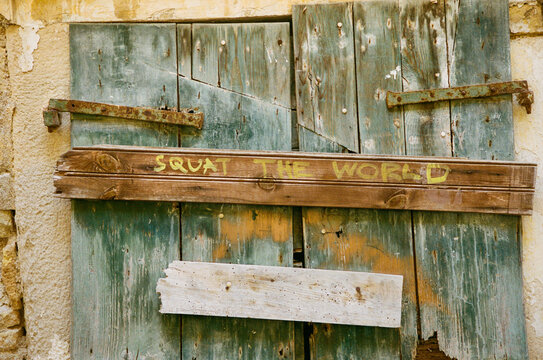 Rustic shuttered window with the words squat the world daubed on it.