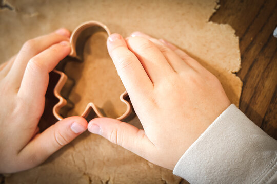Child’s hands using a cookie cutter to shape gingerbread dough on a wooden table during Christmas baking. - Powered by Adobe