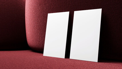 Two blank business cards in vertical format leaning on a luxurious and elegant red sofa