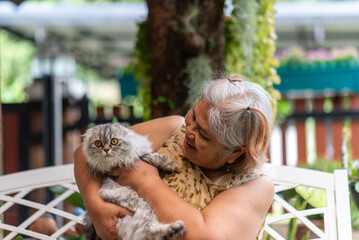 Asian senior woman sitting in garden holding cat and talking with pet