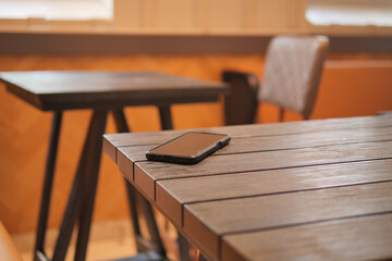 Wooden table with a smartphone placed on it in a cafe. lost smart phone concept