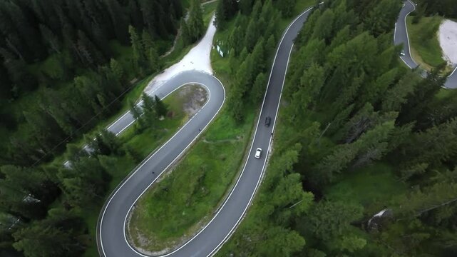 dolomites traffic flowing through tight switchback above dense forest, aerial perspective shows multiple vehicles negotiating hairpin bend, sense of movement, transport logistics and scenic