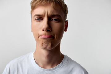 Obraz premium Puzzled man with skeptical expression, furrowed brow and tight lips, white t shirt, neutral background, close up studio shot conveying doubt, hesitation and confusion in a candid moment