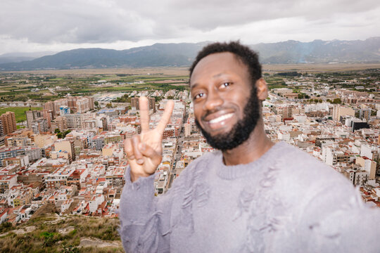 Smiling man taking selfie with peace sign overlooking city