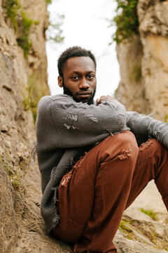 Stylish man with ripped sweater sitting on rocks