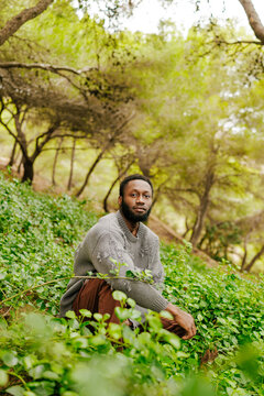 Black man crouching in green forest enjoying nature