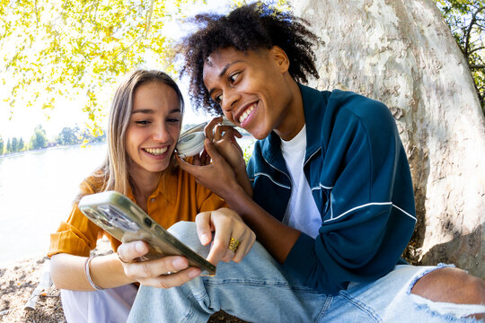 Two friends hanging out in park listening to music sharing headphones
