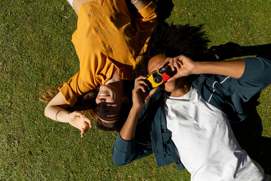 Two friends lying on grass taking picture with disposable camera
