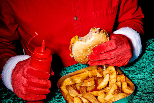 a man in santa gloves is about to add ketchup to a bitten burger