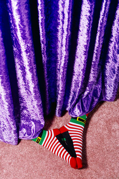 male feet in striped christmas socks hidden under purple curtain
