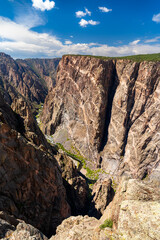 View of the massive Painted Wall in Black Canyon of the Gunnison National Park. White pegmatite dikes create stripes on the dark, sheer cliff. The Gunnison River is visible below
