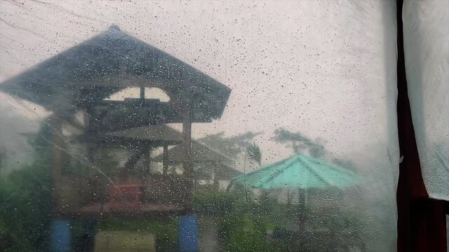 Rain covered plastic windows with blurred view to gazebo and umbrellas during heavy rain