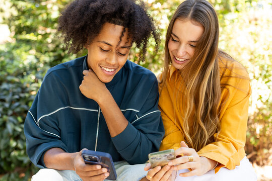 Young couple sitting on bench looking at their smartphones smiling