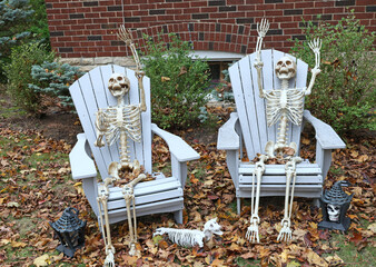 Skeletons sitting in chairs as Halloween decoration in garden of house