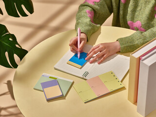 A hand writes on a sticky note atop a notebook at desk